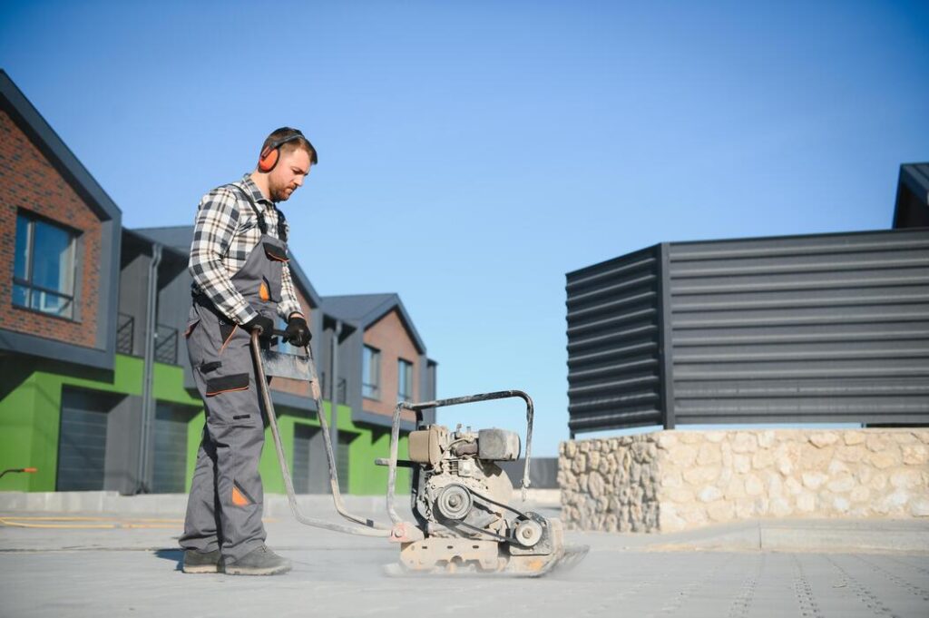 male-worker-using-vibratory-plate-compactor-to-firm-soil-at-worksite-builder-after-laying-of-paving-slabs-compacts-paving-stones-with-a-gasoline-vibratory-compactor